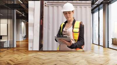 Female container yard worker loading containers box at commercial dock site. Female worker control loading container box from cargo freight ship for import export Wall mural