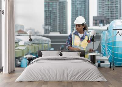 Female engineer working with laptop computer for checks or maintenance in sewer pipes area at construction site. African American woman engineer working in sewer pipes area at rooftop of building Wall mural