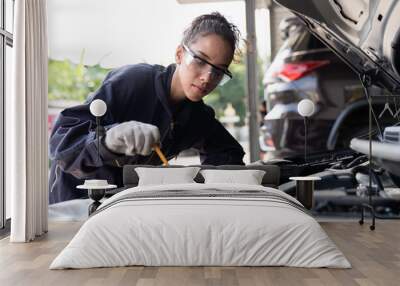 Female mechanic working at the garage. Professional female car mechanic examining, repair and maintenance under hood of car at auto car repair service. Car service and Maintenance concept Wall mural