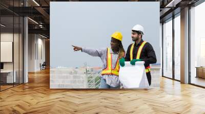 Foreman builder male and female at construction site. Group of foreman construction working at construction site, wearing safety uniform, helmet and holding blueprint structure Wall mural