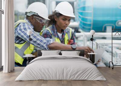 Group of African American engineer working in sewer pipes area at construction site. Male engineer and woman engineer discussing for maintenance sewer pipes, water tank on rooftop of building Wall mural