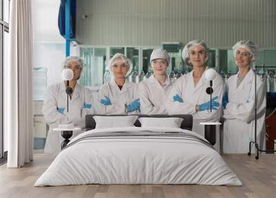 Group of female workers working in mineral water plant. Team of female workers wearing uniform, gloves and hairnet standing together with crossed arms in bottling drinking water factory Wall mural