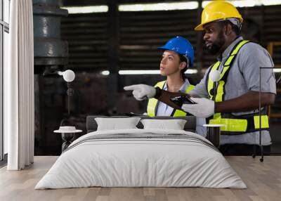 Group of male and female engineer work with digital tablet for check or maintaining heavy metal machine at the industry factory area. Team of technician wear safety uniform working in the factory Wall mural