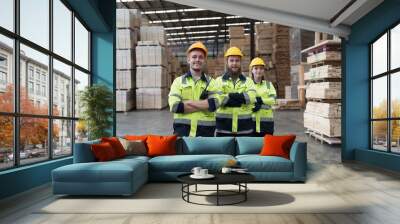 Group of male and female warehouse workers standing together with crossed arms and smiling in industry factory, wearing safety uniform and helmet. Warehouse workers working in warehouse storage Wall mural