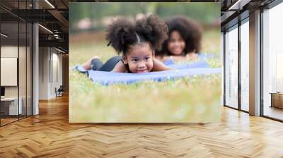 Happy smiling African American little girl lying and doing yoga on roll mat in the park. Kids girl playing and practicing doing yoga outdoor. Little afro girl with curly hairstyle relaxing in nature Wall mural