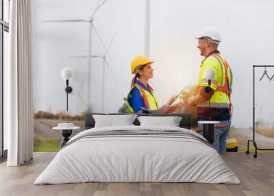 Male and female engineer wearing uniform and helmet discuss while survey the land area at wind turbines farm Wall mural