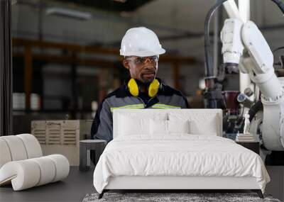 Male engineer holding robot controller for maintenance or repair automatic robotic machine in factory. Male technician worker working with control automatic robot arm system welding in the factory Wall mural