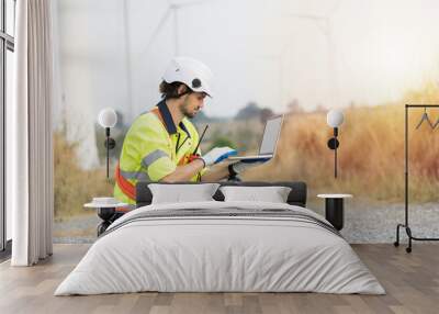 Male engineer wearing uniform and helmet while control or monitoring wind turbines by laptop computer at wind turbines farm Wall mural