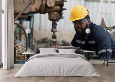 Male factory worker working at work maintenance machine in industrial factory while wearing safety uniform, glasses and hard hat. Black male technician and heavy steel lathe machine in workshop Wall mural