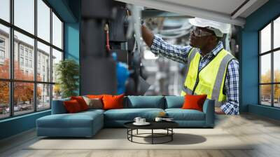 Male plumber engineer working at sewer pipes area at construction site. African American male engineer worker check or maintenance sewer pipe network system at construction sit Wall mural