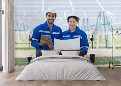 Portrait of two male and female worker using laptop computer working in solar panels power farm standing in front of long rows array of photovoltaic solar cells panels Wall mural