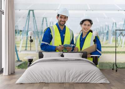 Portrait of two male and female worker using laptop computer working in solar panels power farm standing in front of long rows array of photovoltaic solar cells panels Wall mural