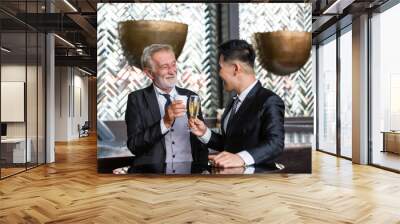 Senior businessman talking, discussing ideas with asian partner in conference room while holding a glass of wine. They are all standing, wearing suits and happy smiling. business, people concept Wall mural