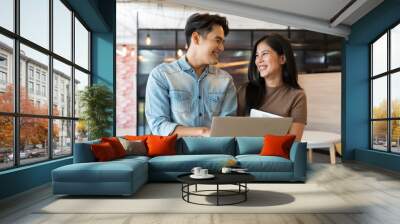 Smiling Asian business man and woman standing discuss and working with laptop computer at the office workspace. Two Asian colleagues man and woman discussing together in the modern office Wall mural