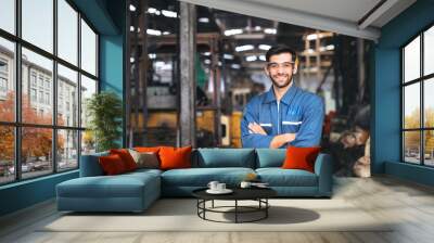 smiling worker in safety glassess standing with arm crossed near industrial equipment manufacturing  Wall mural