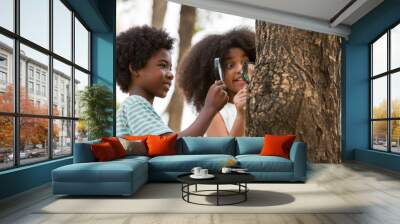 Teenager boy and girl examining the tree stem through magnifying glass. Group of African American children exploring nature on the tree with magnifying glass. Education and discovery concept Wall mural