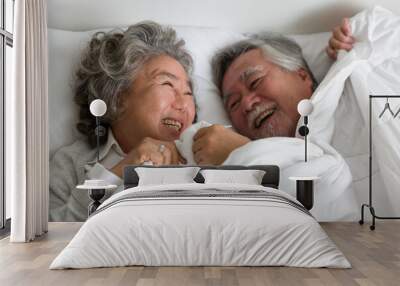 Top view of happy smiling asian elderly couple hugging and sleeping together on bed with white blanket, pillow in the bedroom at home. Retirement, health care, relax and spending time concept Wall mural