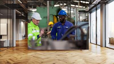 Two engineering male factory workers working and discussing in the industrial factory while wearing safety uniform and hard hat Wall mural