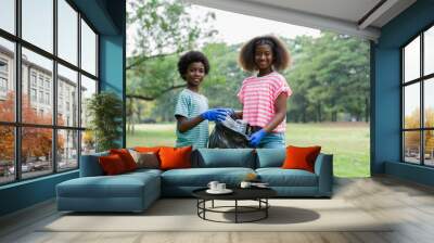 Volunteer children. Cheerful boy and girl in gloves holding black garbage bag with plastic bottles outdoor. Volunteer and charity concept Wall mural