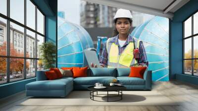 Woman engineer or woman technician work at construction site area. Portrait of African American woman engineer worker standing near sewer pipes or water tank area at construction site Wall mural