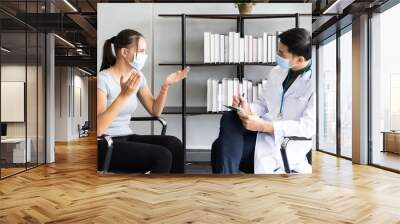 Woman wearing face mask sitting on the armchair and talking to the professional psychologist while wearing face mask conducting a consultation and making notes during coronavirus or COVID 19 outbreak Wall mural