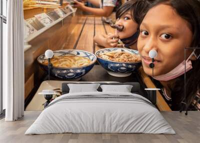 Asian teen girl with his little brother waiting in queue for having dinner together at a Japanese restaurant with noodles menu Wall mural