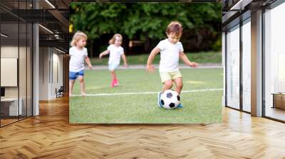 Football game: team of toddlers playing soccer on green field: three children, two boys (one is barefoot) and girl playing at stadium, smiling little boy dribbling ball is running in front place Wall mural