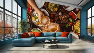 a large wooden table generously covered with delicious national dishes, with friends sitting and drinking light beer from glasses Wall mural