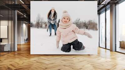 Happy mother and baby daughter having fun under sunny winter snow, holiday season Wall mural