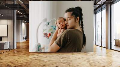 Loving mother carying of her newborn baby at home. Bright portrait of happy mum holding cute infant child on hands. Mother hugging her little 1 months old daughter. Wall mural