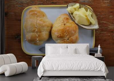 Two fresh croissant on dish with butter in cup and knife, French bread on brown wooden table Wall mural