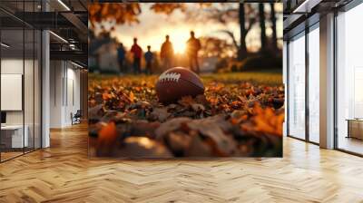 A football lies on a bed of autumn leaves, while children play in the background under the golden glow of the setting sun. Wall mural