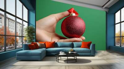 Isolated on Christmas green color background with side space for letters a person holding a shiny Christmas bell ornament with a red ribbon Stock Photo with copy space Wall mural