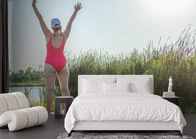 portrait of a young woman in a swimsuit on the beach standing from the back with her hands up over h Wall mural