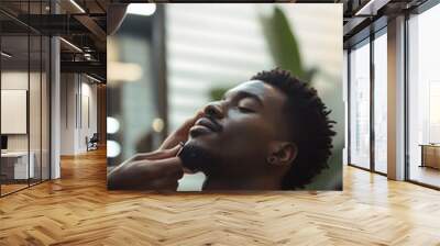 A young black man sits relaxed in a barber shop while getting a haircut, enjoying the experience with a content expression on his face Wall mural