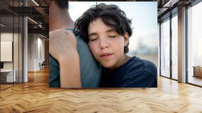 The teenage boy snuggles with tenderness to the strong shoulder of the father, the child seeks protection and support from the parents Wall mural