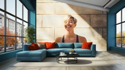 An athletic woman smiles confidently against a textured wall, showcasing a healthy lifestyle and positive energy Wall mural