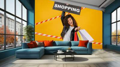 black woman with shopping sign and colorful shopping bags isolated over yellow with signal tape Wall mural