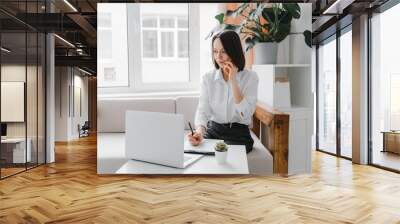 Young businesswoman talking on the phone at home or office. Wall mural