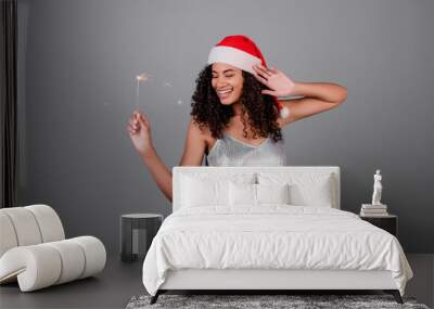 happy black woman with sparkling sparklers wearing santa hat and dress isolated over grey Wall mural