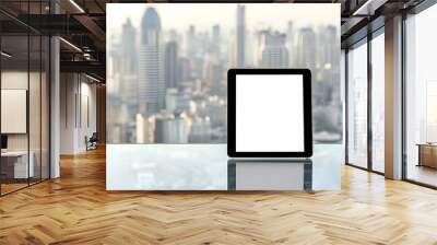 Minimalist photography of a tablet positioned on a glass table with a blurred cityscape in the background highlighting urban life and technology Wall mural