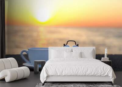 Morning sunrise on the beach. White cup and alarm clock on stone breakwater with sea background and sunshine. Space for text. sunrise beach breakfast. Good morning let's start a new day concept Wall mural