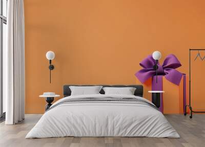 Orange colored gift box with a purple bow on an orange background. Halloween style gift box.  Wall mural