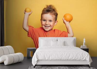 Studio shot of a smiling boy holding a fresh lemon and orange on a yellow background. The concept of healthy baby food, vitamin C. Wall mural