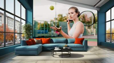 young tennis player woman tossing ball up with racket on court Wall mural