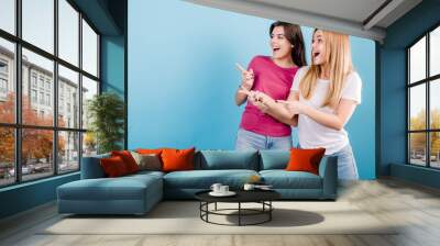 young women pointing fingers at copy space on blue background Wall mural