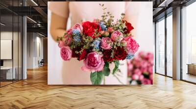 Very nice young woman holding huge beautiful blossoming bouquet of fresh roses, muskari, eucalyptus in red and magenta colors on the grey background Wall mural