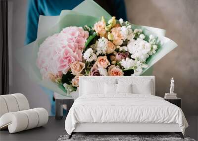 very nice young woman in a blue sweater holding a beautiful blossoming flower bouquet of fresh hydrangea, roses, carnations, matthiola, in pink and pastel cream colors on the grey wall background Wall mural