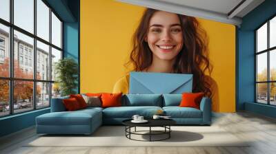 Cheerful Woman with Envelope, Radiant young woman holding a light blue envelope with a bright smile, her cheerful demeanor enhancing the vibrant yellow background Wall mural