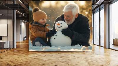 Handsome white-haired grandfather and cute little boy making a snowman on a sunny winter day.  Wall mural